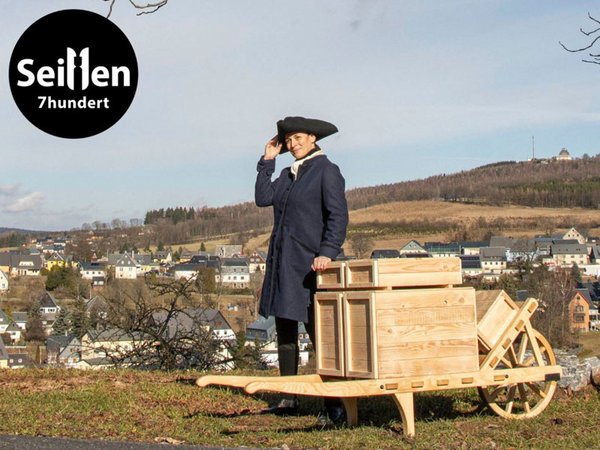 Johanna Kaden als Johann Friedrich Hiemann mit Schiebock vor der Kulisse des Spielzeugdorfs Seiffen. Foto: Dregeno