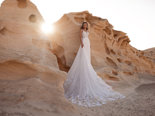 Frau im A-Linien-Brautkleid Malika von DAMA Couture mit floraler Spitze und langem Rock vor einer Felswand.